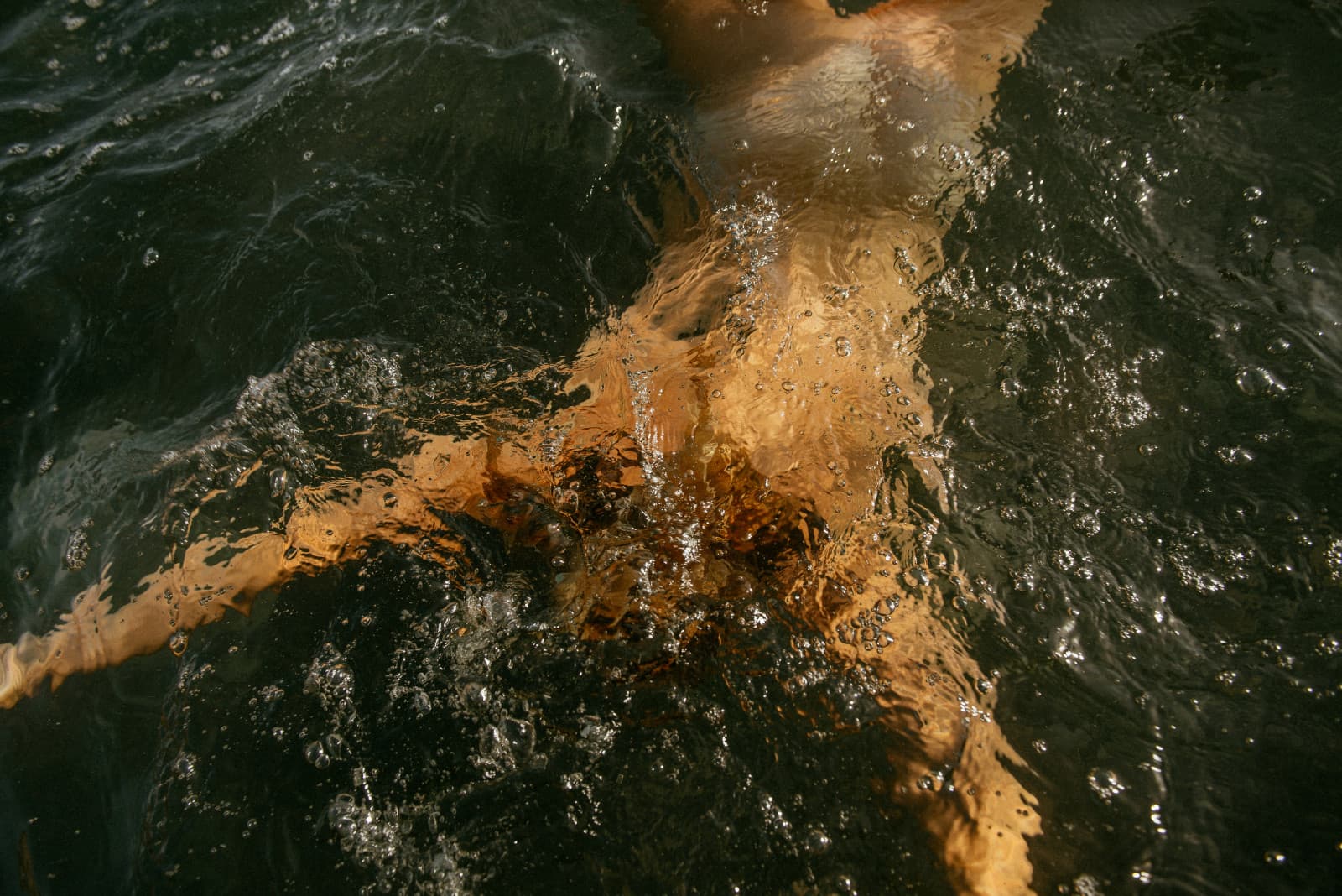 An overhead view of a swimmer beneath rippling, sunlit green water
